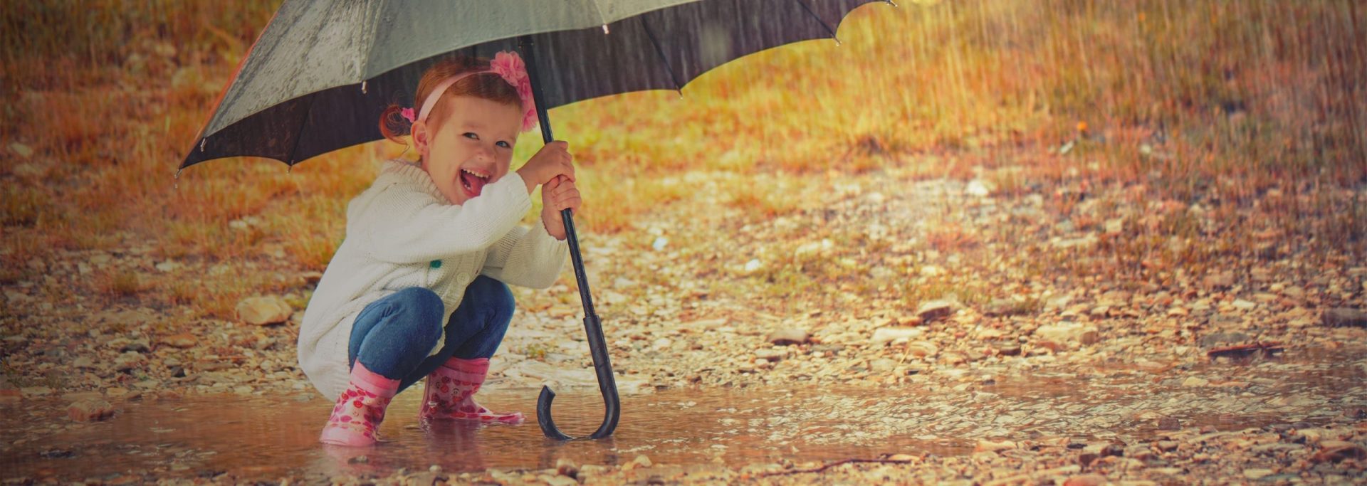 Insurance | Child playing in the rain in wellies under an umbrella